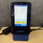 Blue electronic device with a screen displaying 'piccolo xpress' on a wooden surface.